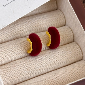 Detalle de pendientes de terciopelo rojo en forma de C con bordes dorados ondulados