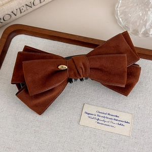Detail view of large brown suede bow hair claw clip with golden engraved love metal tag