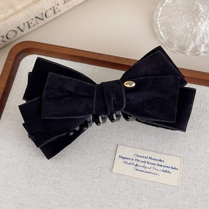 Detailed view of elegant black velvet bow hair clip with gold metal tag on fabric tray