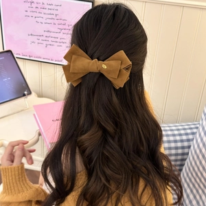 Brown suede bow hair clip with gold logo shown on an elegant half-up hairstyle