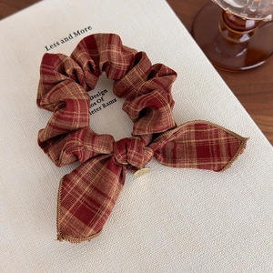 Macro shot of vintage red brown plaid bow scrunchie with metal charm on white book