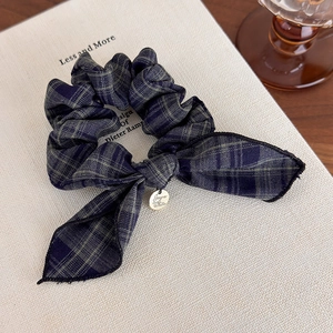 Close-up of a plaid navy and green scrunchie with bow and gold metal pendant