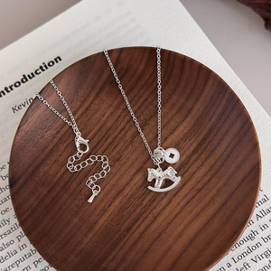 Silver rocking horse necklace with traditional round pendant on a dark wooden base