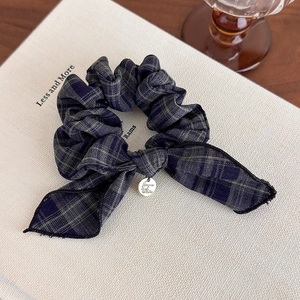 Detail view of navy blue plaid bow hair scrunchie with silver metal charm on book