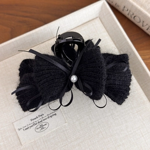 Dettaglio di un fermaglio per capelli in peluche nero con fiocco di velluto e perla bianca
