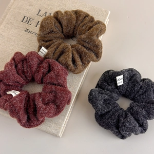Three wool blend scrunchies in brown, dark red, and grey on a cream book for winter hair