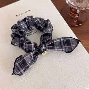 Detail of checkered bow hair scrunchie with a gold logo tag on a textured book surface