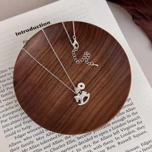 Detailed shot of silver rocking horse pendant and coin charm on a wooden tray