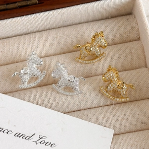 Detail view of gold and silver rocking horse stud earrings with zircon inlay in a jewelry box
