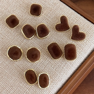 Macro shot of assorted brown velvet earrings in geometric shapes on a beige linen base