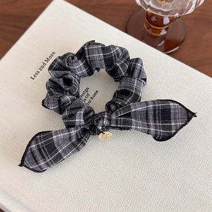 Detail of vintage plaid bow hair tie with gold charm on a textured book surface