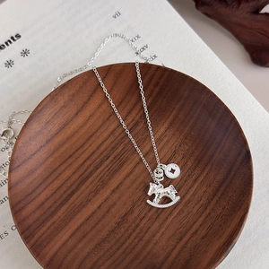 Detailed view of silver rocking horse necklace on a rustic wooden tray over a book