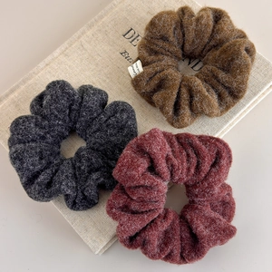 Close-up of wool texture scrunchies in grey, caramel, and burgundy on a beige book