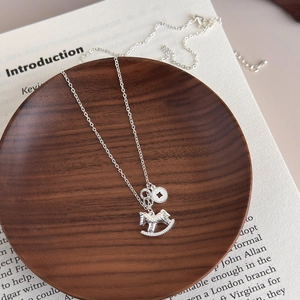 Detailed close-up of a silver rocking horse and coin pendant necklace on a wooden tray