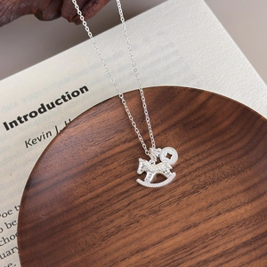 Silver rocking horse necklace with coin pendant on a vintage book display
