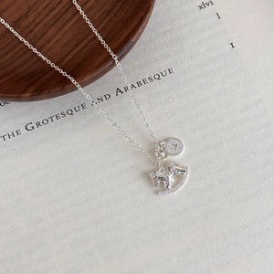Macro detail of silver rocking horse pendant with hammered texture on a wooden background