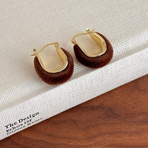 U-shaped gold hoop earrings with brown velvet finish on a white design book background