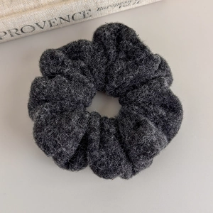 Detailed texture of a dark grey fuzzy wool scrunchie next to a decorative linen book