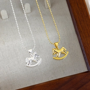 Close-up of gold and silver rocking horse necklaces with hammered texture on linen tray