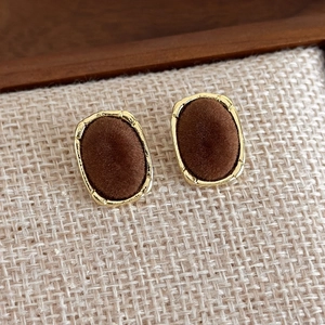 Close-up of vintage oval stud earrings with golden frames and dark brown velvet texture