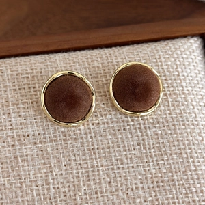 Detail of round brown velvet stud earrings with elegant gold metallic borders