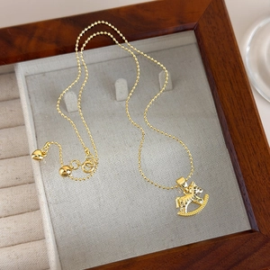 Detail of a golden rocking horse pendant on a ball chain necklace with heart charm
