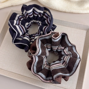 Two knitted scrunchies in navy blue and brown stripes on a textured display tray