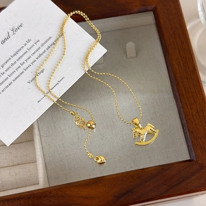 Detailed shot of golden rocking horse pendant on a bead chain over a wooden jewelry tray