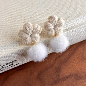 Détail de boucles d'oreilles fleur en laine avec pompons blancs doux dans un décor chaleureux