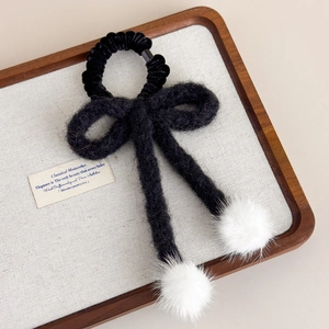 Dettaglio dell'elastico per capelli nero lavorato a maglia con pompon bianchi su vassoio