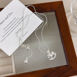 Macro shot of silver rocking horse pendant with delicate bead chain on a jewelry tray