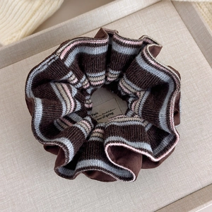 Detailed close-up of brown oversized scrunchie with striped knit texture on a tray