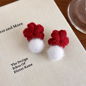 Vue détaillée de boucles d'oreilles fleurs tricotées rouges avec pompons blancs sur un livre