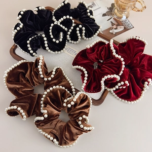 Detailed view of four velvet scrunchies with white faux pearls in red, black, and brown