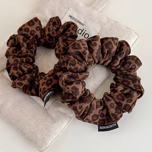 Two leopard print suede scrunchies with handmade labels on minimalist fabric background