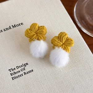 Détail des boucles d'oreilles fleurs tricotées jaunes avec pompons blancs doux
