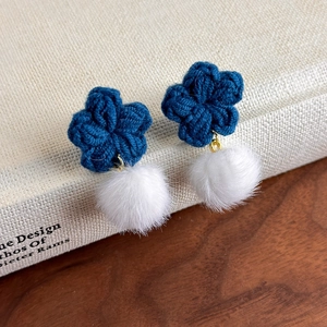 Détail de boucles d'oreilles fleurs tricotées bleu foncé avec pompons blancs doux
