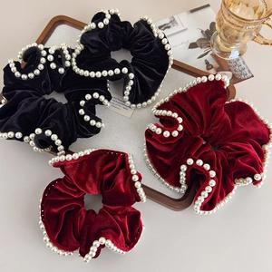 Detailed close-up of velvet pearl scrunchies in black and burgundy on a tray