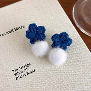 Macro détaillée de boucles d'oreilles fleur au crochet bleu marine avec pompons blancs