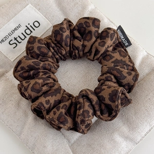 Suede leopard print hair scrunchie with handmade label on beige canvas background