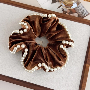 Detail of caramel velvet scrunchie with white faux pearl trim in a wooden tray