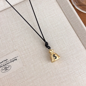 Detailed close-up of a gold money bag pendant with black cord on a beige woven tray