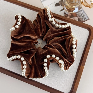 Detailed view of vintage brown velvet scrunchie with white faux pearls on wooden tray