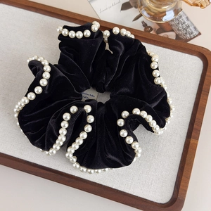 Detailed view of a black velvet scrunchie with white pearl trim on a textured linen background