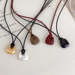 Five minimalist brushed metal trapezoid pendant necklaces on black cord in varied colors