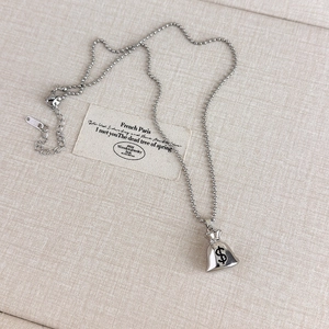 Detailed close-up of a silver money bag pendant necklace with dollar symbol on textured fabric