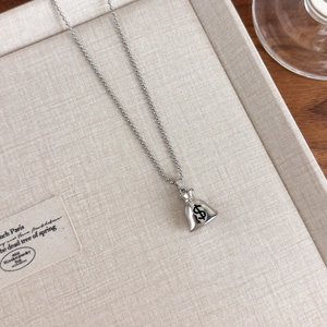 Macro detail of silver money bag pendant necklace with dollar symbol on textured tray