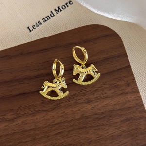 Detail of gold rocking horse earrings with hammered texture on a wooden jewelry tray