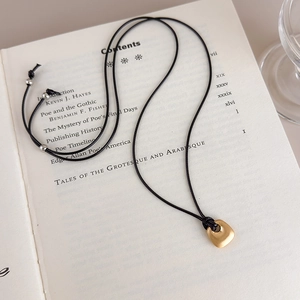 Minimalist matte gold pebble pendant on black cord styled on an open vintage book