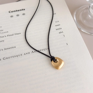 Detail of matte gold pebble pendant on black cord over a vintage book page